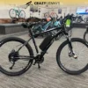 An EG Kyoto (Demo) electric bike is displayed in a showroom with several other bikes in the background. The bike is black with thick tires, a central battery, and appears to be a hybrid mountain style. Serving as a demo model, the showroom showcases Crazy Lenny's Electric Bikes logo at the top. An EG Kyoto (Demo) electric bike is displayed in a showroom with several other bikes in the background. The bike is black with thick tires, a central battery, and appears to be a hybrid mountain style. Serving as a demo model, the showroom showcases Crazy Lenny's Electric Bikes logo at the top.