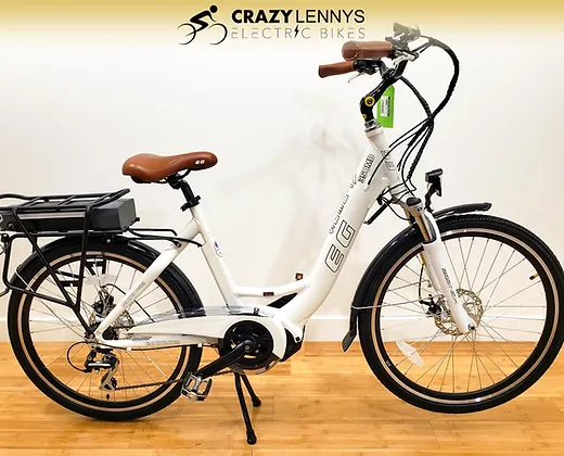 An electric bicycle on display with a white frame, brown seat, and black handlebars. It features a rear rack with a battery pack, front and rear fenders, and a kickstand. The EG Athens 350MD Mid Drive model also boasts a powerful mid-drive motor. The background includes the logo of "Crazy Lenny's Electric Bikes.