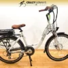 A white EG Athens 350DX Hub Drive electric bicycle with brown handlebars and seat is displayed against a plain background. The bike, featuring a hub drive, front light, rear cargo rack with battery, and Crazy Lenny's Electric Bikes branding on the top, sits on a wooden floor that adds warmth to the photo.