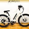 A white Serfas eDASH with thick tires and a black saddle is placed on a wooden floor against a white wall. The logo "CRAZY LENNY'S ELECTRIC BIKES" is displayed at the top in black text on a beige background, just above the sleek Serfas handlebars.