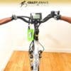 Front view of a white EG Athens 350DX Hub Drive with "ATHEN" written on the frame. The bike, featuring a digital display on the handlebars, which are covered with brown leather grips. A green tag hangs from the handlebars. A sign above reads "CRAZY LENNY'S ELECTRIC BIKES.