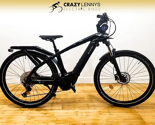 A sleek black electric bike with a modern design, featuring thick tires, a front suspension fork, disc brakes, and a mounted battery pack on the frame. Branded as "Crazy Lenny's Electric Bikes," this Bianchi e-Omnia T-Type model is displayed indoors on a wooden floor with elegance and style.