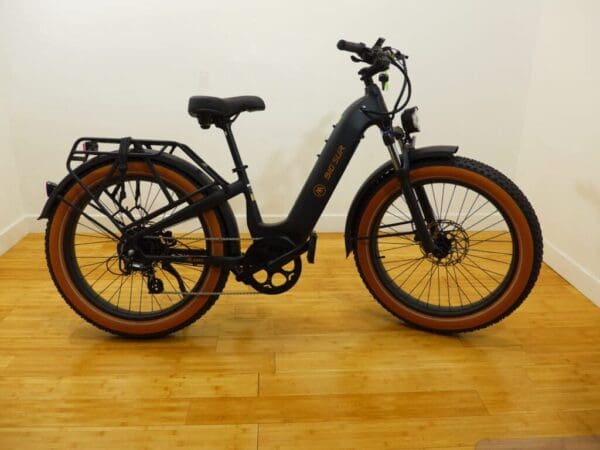 Black electric bike with tan tires on wood floor.