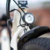 Close-up of the Emojo Bull E-Trikes headlight mounted above its front tire and black fender, with a blurred outdoor background. Close-up of the Emojo Bull E-Trikes headlight mounted above its front tire and black fender, with a blurred outdoor background.