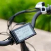 Close-up of the Emojo Bull E-Trikeโs digital display on the handlebars, presenting speed, battery status, and distance. The background reveals a blurred pathway bordered by greenery. Close-up of the Emojo Bull E-Trikeโs digital display on the handlebars, presenting speed, battery status, and distance. The background reveals a blurred pathway bordered by greenery.