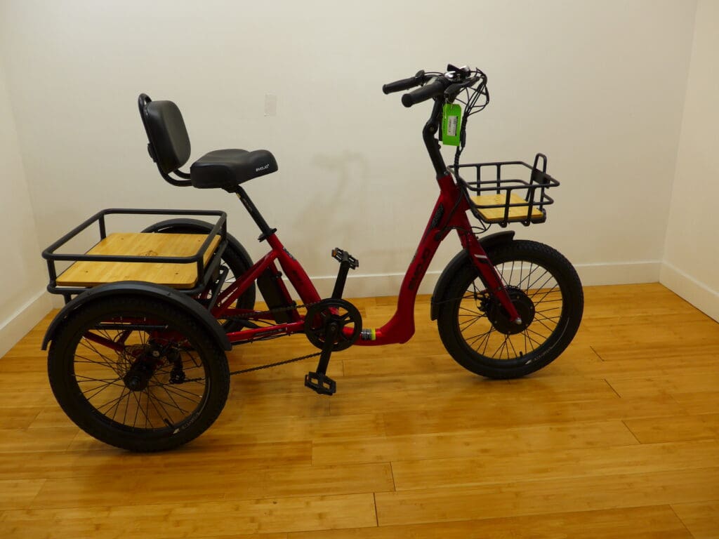 Red electric cargo trike with baskets indoors.