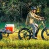 hunnting-1-ebike-5-322640_1800x Person biking with trailer carrying cooler in field.