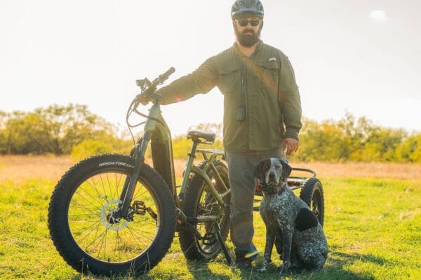 Man with bicycle and dog in sunny field.