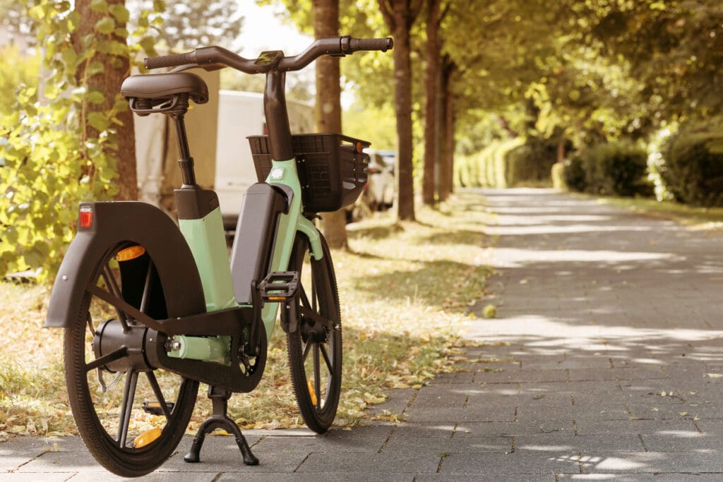Electric bike parked on sunny tree-lined path.