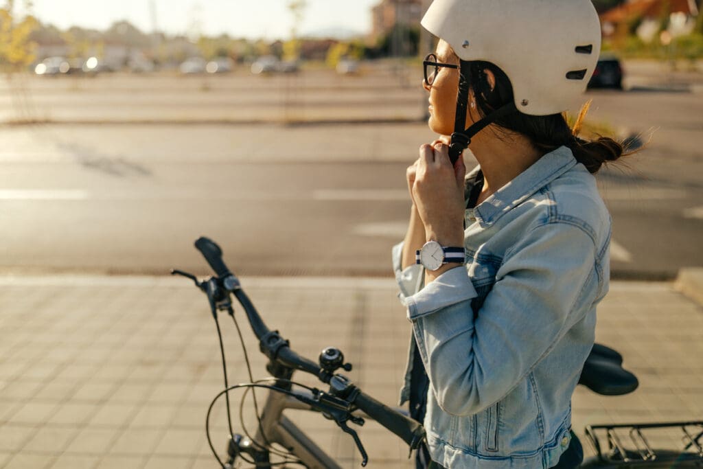 Woman wearing helmet standing with bicycle outdoors.