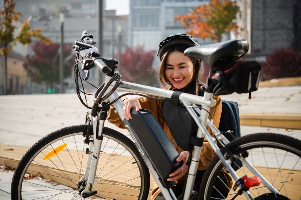 Woman with bike, adjusting battery outdoors.
