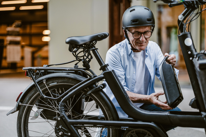 Man wearing helmet adjusting electric bicycle battery.