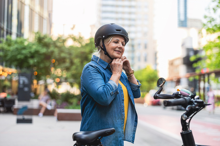Woman securing bike helmet in city street.