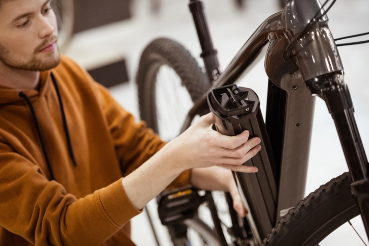 Person adjusting battery on electric bicycle indoors.