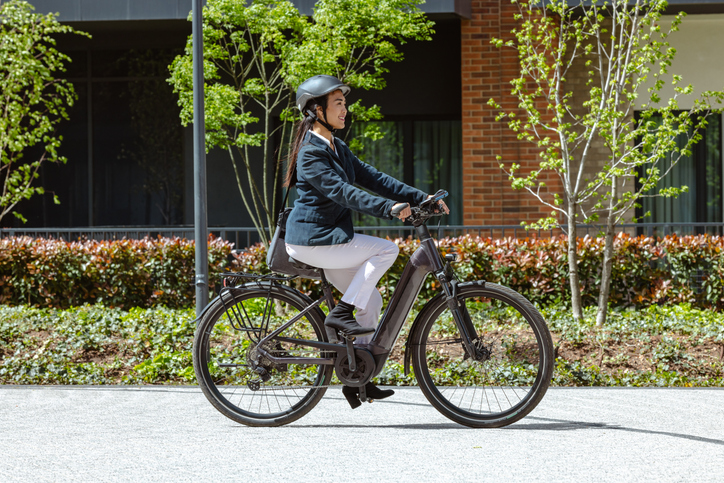 Person riding electric bicycle outdoors in city setting.