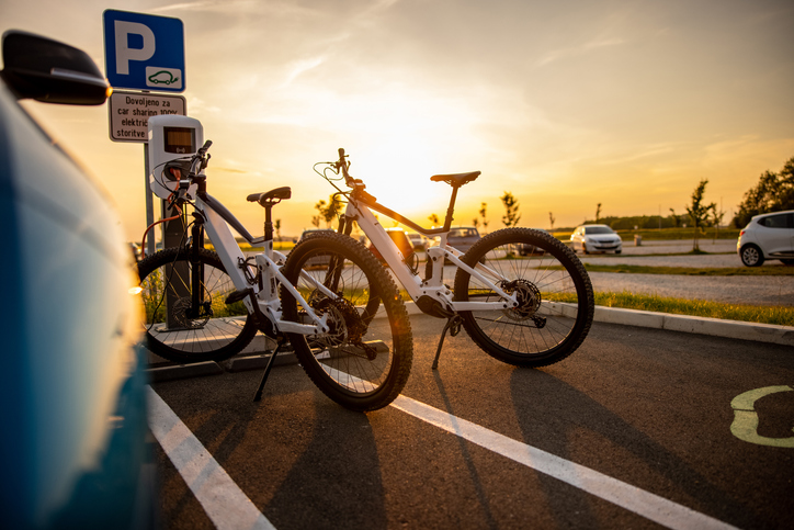 Electric bikes parked by charging station at sunset.