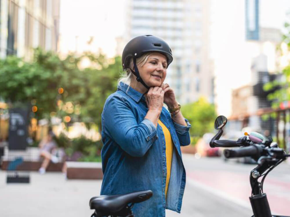 Woman adjusting helmet next to bicycle in city.