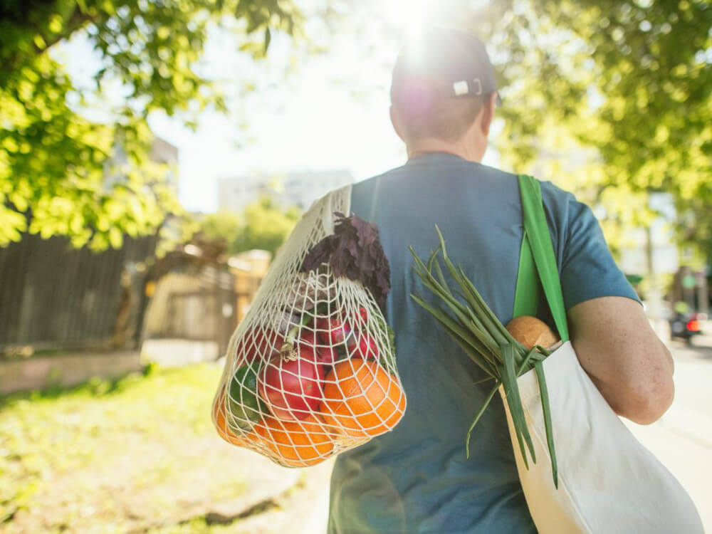 Person carrying fresh produce in reusable bags.