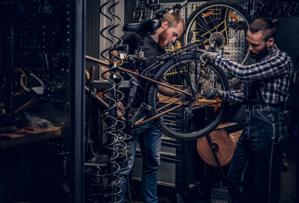 Two men repairing a bicycle in a workshop.