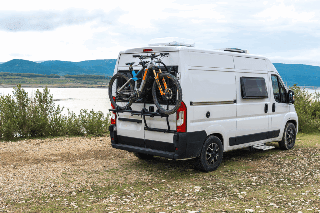Camper van with bicycles near lake and mountains.