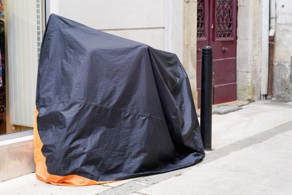 Covered object with black tarp on sidewalk