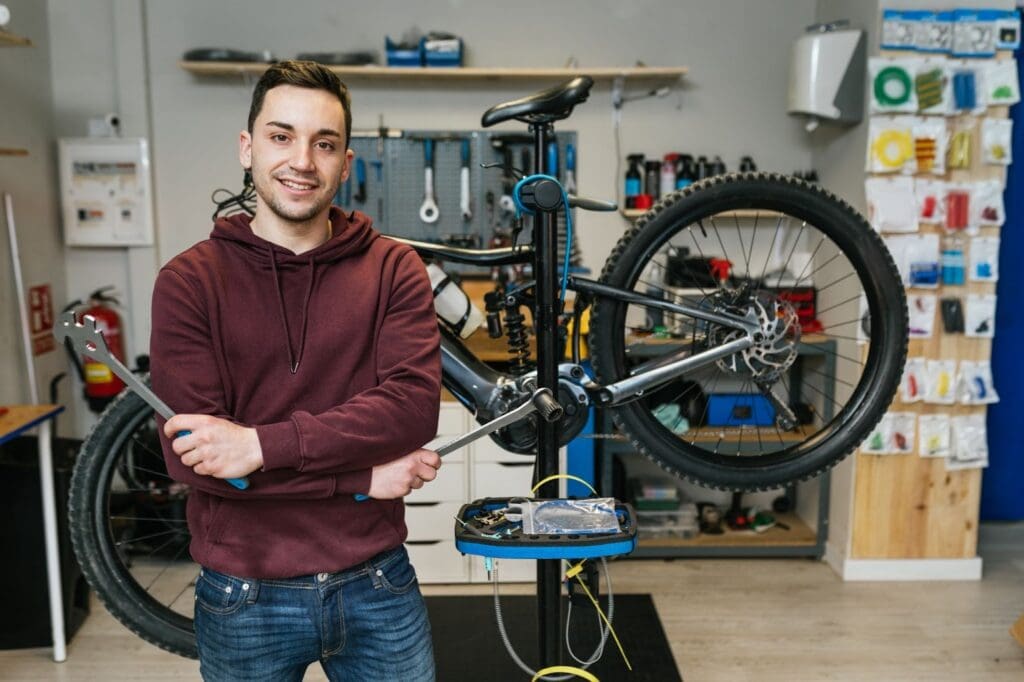 Bicycle mechanic smiling in repair shop with tools.