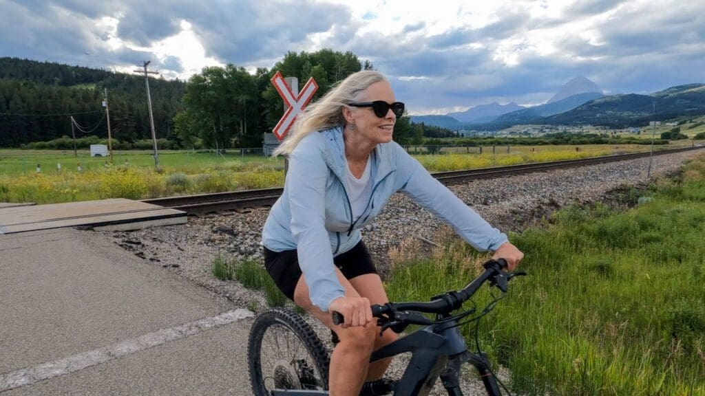 Woman biking near railroad and mountains.