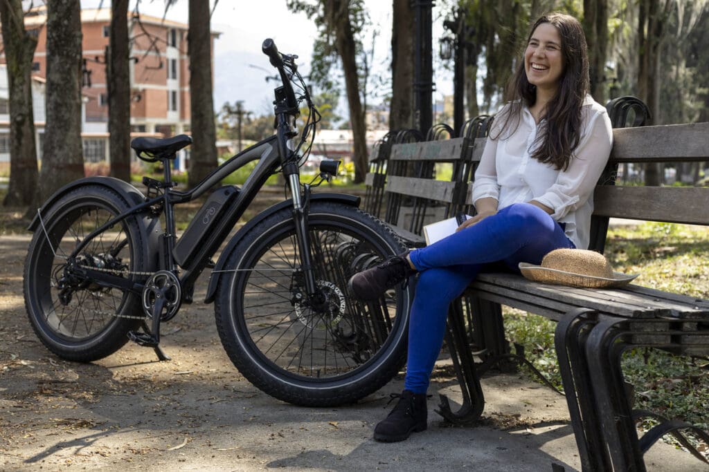 Woman sitting on bench with electric bike in park
