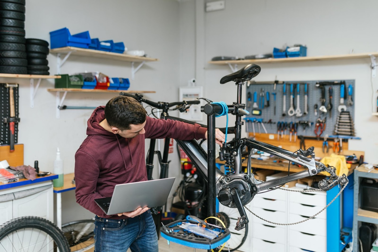 Mechanic repairing bicycle with laptop in workshop.