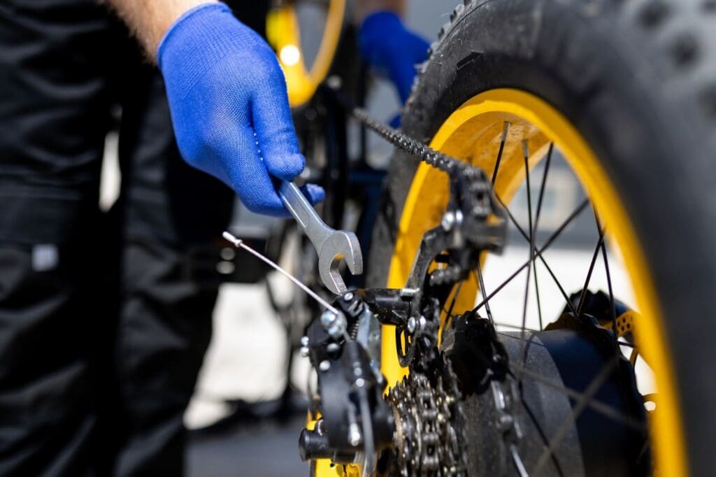 Gloved hands fixing bicycle chain with wrench.
