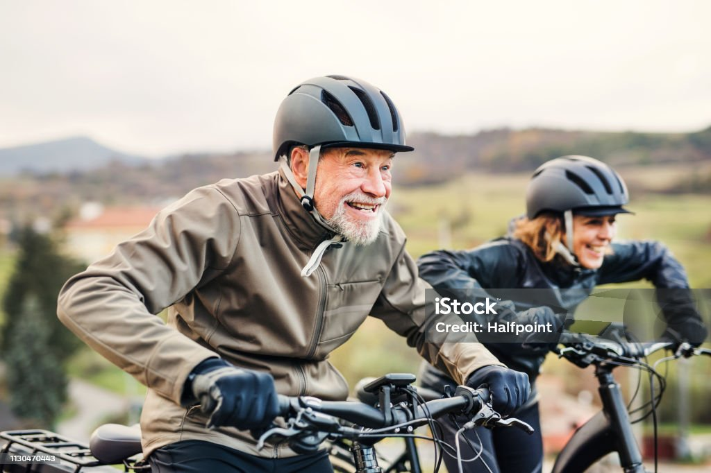 Elderly couple biking with helmets in countryside