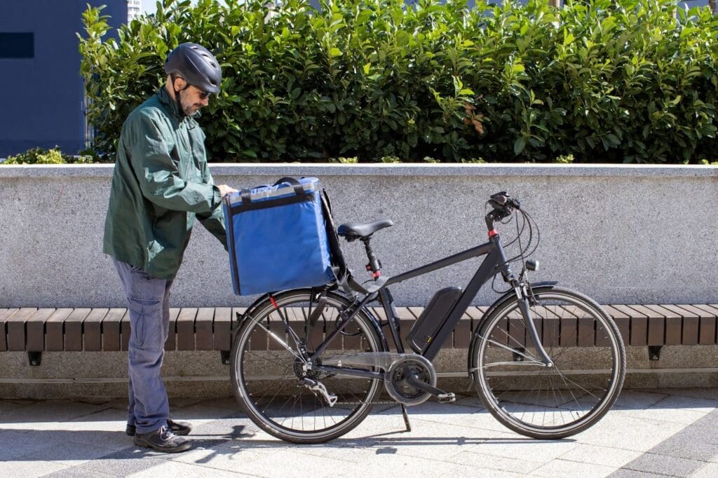 Man with helmet secures delivery bag on bicycle.