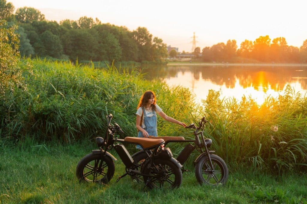 Woman with electric bikes by lakeside at sunset