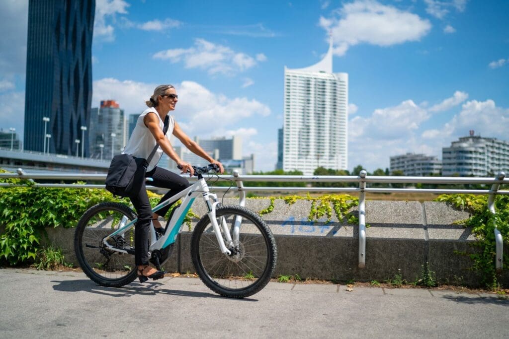 Woman biking in city with tall buildings background.