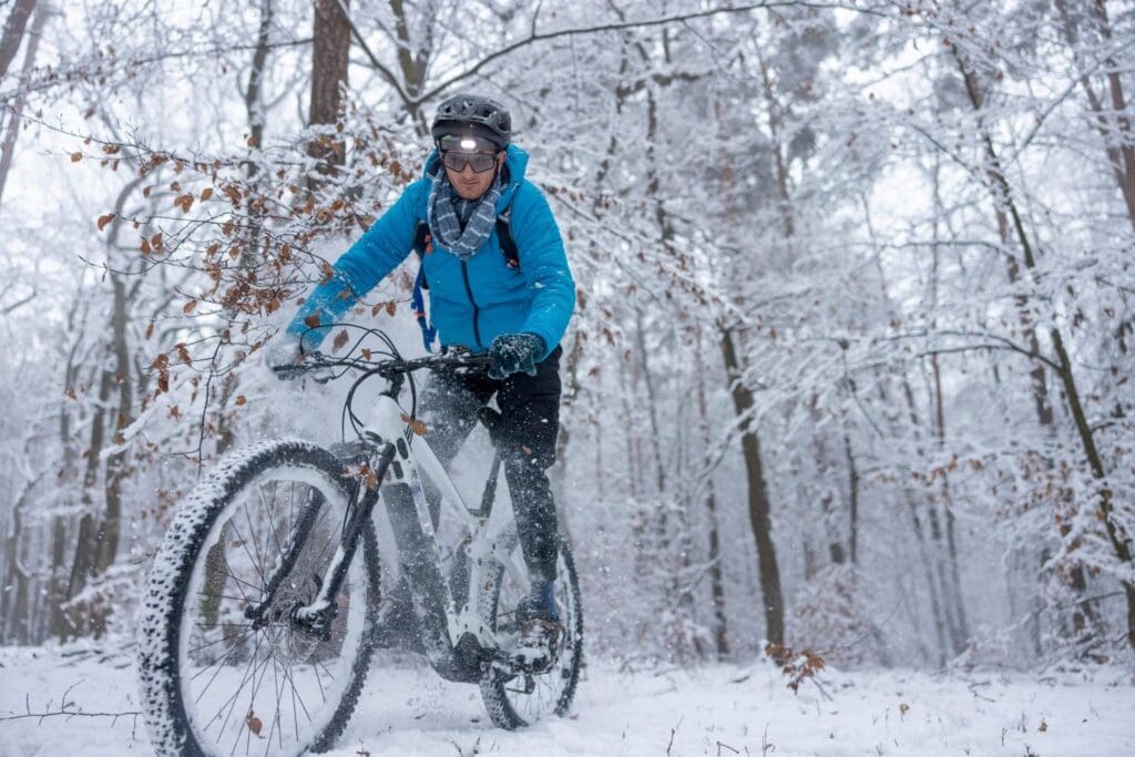 Cyclist biking through snowy forest trail in winter.