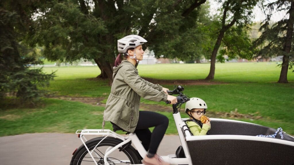 Woman riding cargo bike with child in park