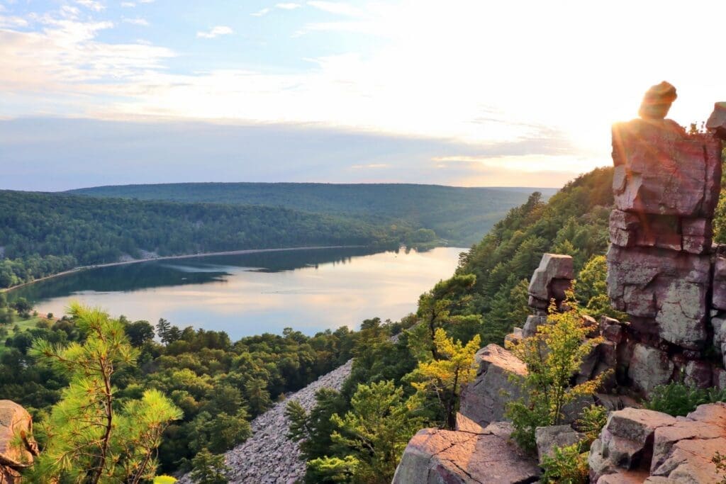 Rocky cliff overlooking forested lake at sunset