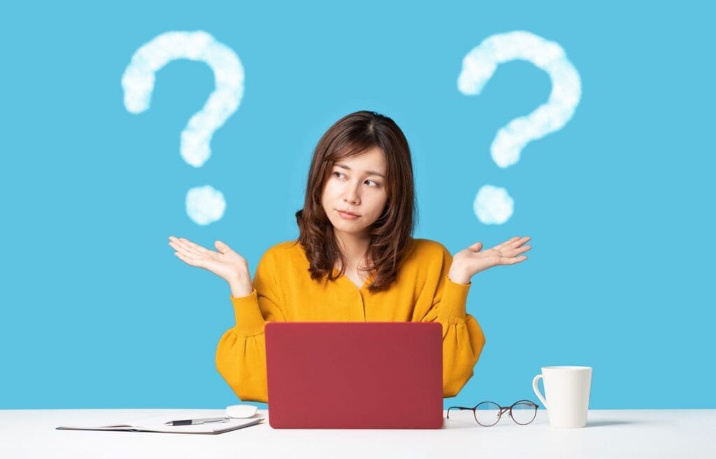 Confused woman shrugging at laptop with question marks