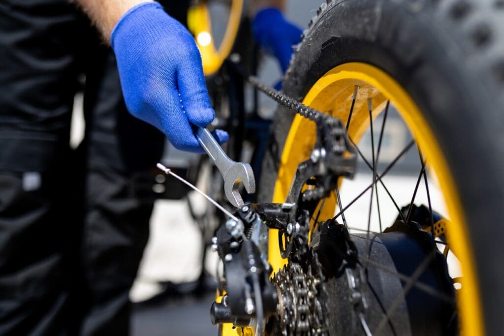 Mechanic adjusts bicycle rear derailleur with wrench