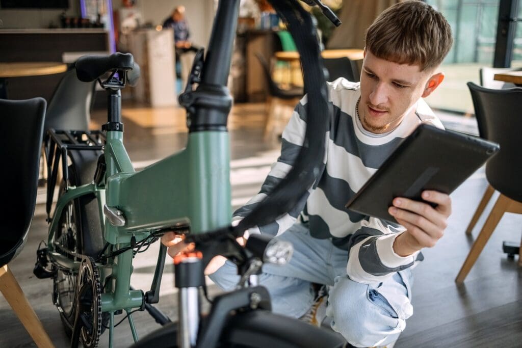 Man inspecting folding electric bicycle with tablet indoors