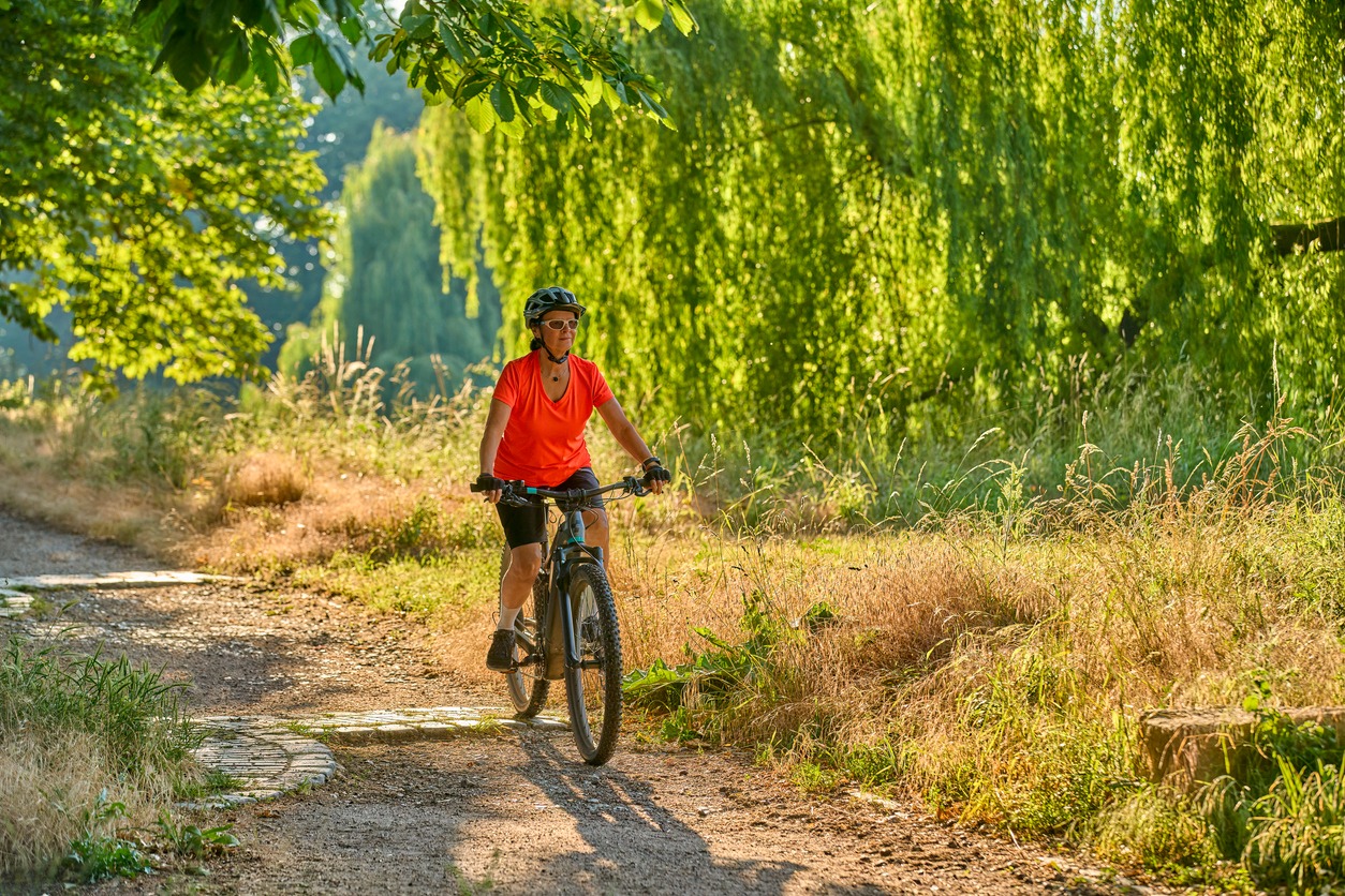 Woman cycling on sunlit forest trail