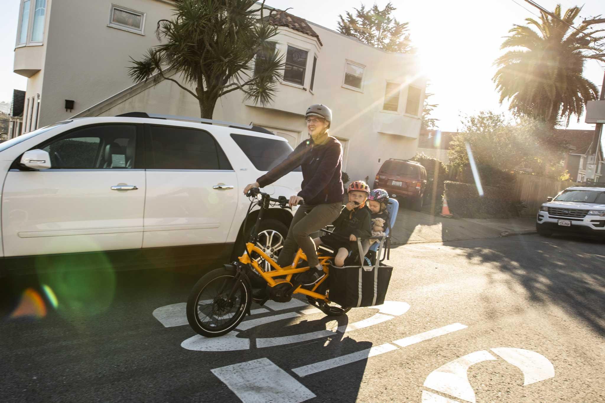Adult biking with two children on cargo bike